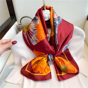 Foulard de luxe en soie à motif lys bordeaux et orange noué en ruban sur un pull blanc