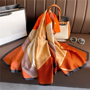Detail of a luxury geometric silk scarf with houndstooth pattern draped on a leather sofa
