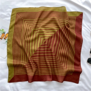 Close-up of olive green and burgundy geometric silk scarf on a white textured background