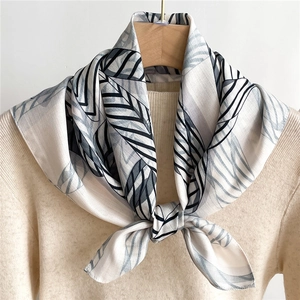 Carré de soie imprimé feuilles double face noué sur un pull beige avec cintre en bois