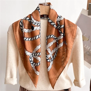 Détail d'un foulard en soie à motif corde orange noué sur un pull en maille crème
