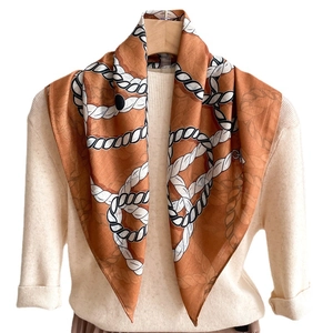 Écharpe orange caramel double face avec motif de corde sur un pull en maille crème