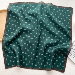 Detailed view of dark green silk square scarf featuring ivory leaf patterns and brown trim