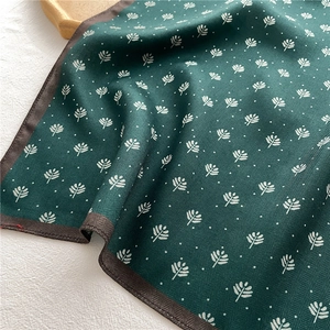 Detail of dark green herringbone silk scarf with white leaf pattern and brown stitched hem