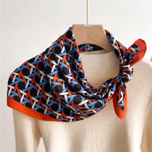 Elegant geometric woven silk scarf in orange and blue displayed on a beige sweater