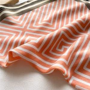 Detailed close-up of geometric orange and white pattern scarf with modern silk texture