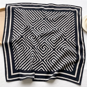 Detail of a black and white square scarf with geometric maze pattern and striped borders