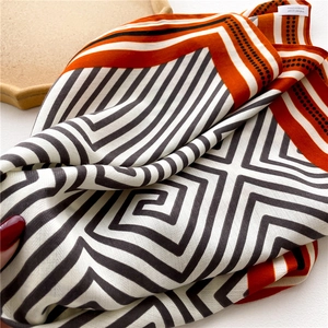 Detailed view of geometric striped silk scarf texture and elegant orange dot border