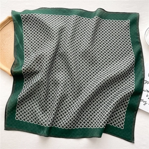 Détail d'un foulard en soie vert avec motif de chaîne blanche sur plateau en bois