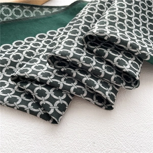 Gros plan d'un foulard en soie vert foncé avec motifs de chaînes et texture sergée fine