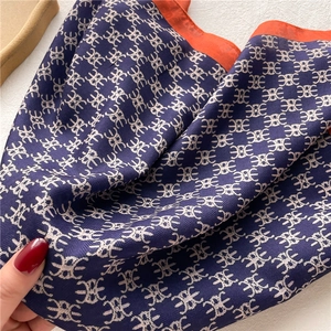 Close-up of navy blue and orange silk scarf featuring abstract geometric patterns and twill texture