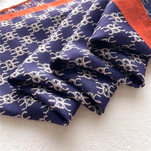 Close-up of a double-sided purple square scarf with letter patterns and orange borders