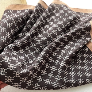 Close-up of brown monogram silk scarf showing detailed herringbone texture and rolled hem