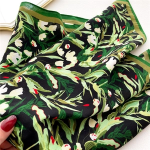 Detail of floral print silk scarf with green leaves on black fabric and contrast hem