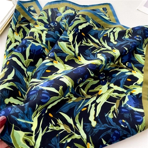 Macro detail of floral silk scarf showing vibrant blue flowers and green leaf patterns