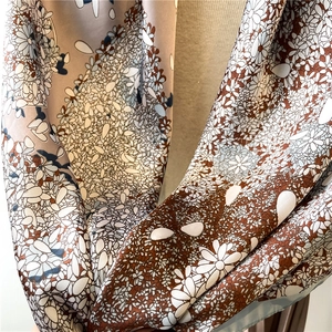 Detail of silk-like satin scarf featuring delicate white daisy prints on light brown fabric
