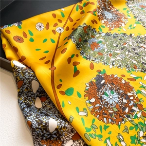 Detailed close-up of yellow silk scarf featuring white daisy prints and floral patterns