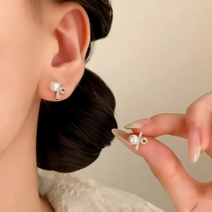 Elegant pearl stud earrings with sparkling bow accent shown on ear for minimalist style