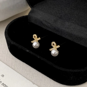 Macro shot of elegant pearl stud earrings with gold crystal knot on black velvet