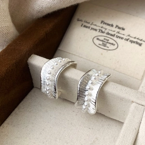 Detail of silver C-shape earrings featuring textured finish and vertical pearl inlay