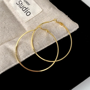 Close-up of elegant large thin gold hoop earrings on textured canvas background