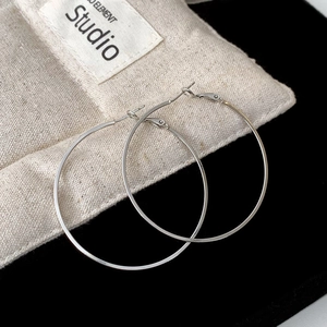 Detail view of large silver hoop earrings on a minimalist linen pouch background