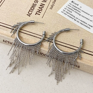 Dettaglio di orecchini a cerchio argento con lunghe nappe di perline su sfondo vintage