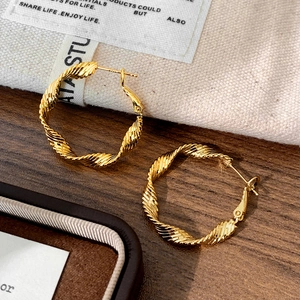Detailed close-up of golden twist hoop earrings with spiral texture on a wooden surface