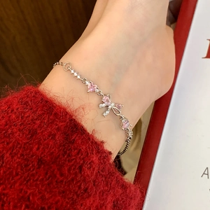Bracelet argenté avec gemmes cœurs roses et nœud scintillant sur un pull en maille rouge