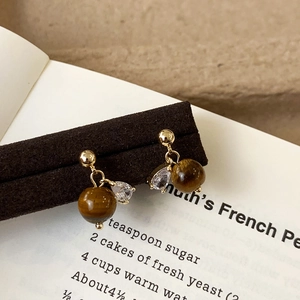 Detail of vintage gold earrings with tiger eye beads and teardrop zircon on a dark plate