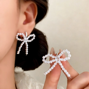 Elegant white pearl bow earrings with silver metal base shown in a close-up lifestyle shot