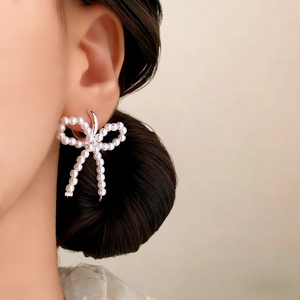 Elegant French style bow pearl earrings featuring polished silver metal on female model