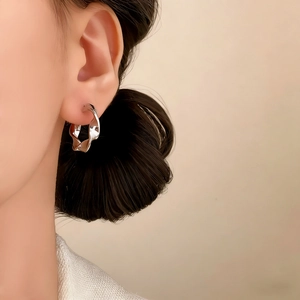 Boucles d'oreilles créoles torsadées géométriques plaquées argent sur un modèle