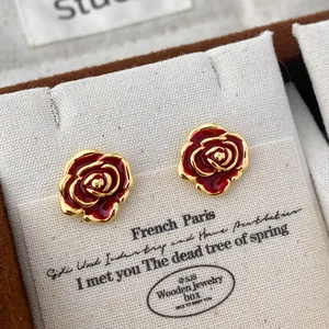Macro detail of retro red enamel rose studs on a white card with premium gold finish