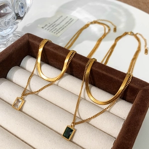 Double-layered gold necklace featuring a flat snake chain and emerald gemstone pendant