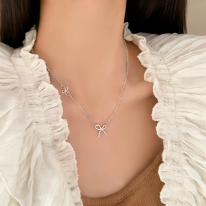 Elegant silver bow pendant necklace with delicate floral charms on model