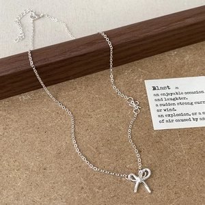 Elegant silver bow pendant necklace with dainty chain accents on a modern minimalist backdrop