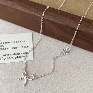 Elegant silver bow pendant necklace with floral accents on a natural rustic background