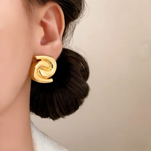 Elegant gold spiral stud earrings featuring a textured swirl design on a female model