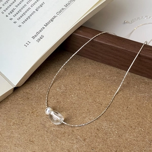 Close-up of minimalist silver chain necklace with clear oval bead on rustic wood background