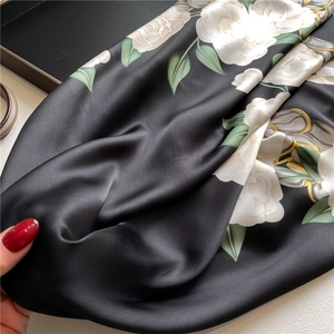 Macro view of silky black floral satin scarf featuring white rose prints and soft luster