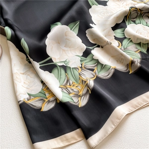 Detail of elegant black floral silk scarf with large white rose and golden edges