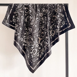 Close-up of black and white paisley silk scarf draped on a minimalist metal hanger