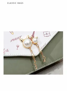 Detail of cat-shaped gold charms with pearls on a patterned crossbody bag