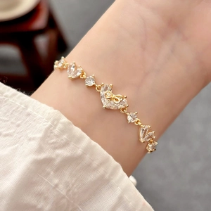 Elegante bracciale dorato con zirconi a cuore e ciondolo a fiocco indossato al polso