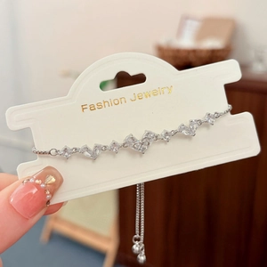 Dettaglio del bracciale a cuore regolabile con zirconi e fiocco su cartoncino