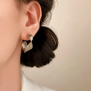 Elegant gold twisted ribbon stud earrings with textured metallic finish on female model