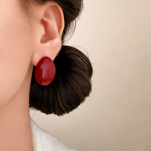 Minimalist red oval stud earrings in glossy finish shown on model for daily fashion look