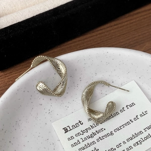 Detail of twisted champagne gold C-shape earrings with beaded edges on a white plate