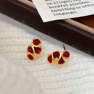 French vintage style gold wavy stud earrings with red enamel on a textured fabric